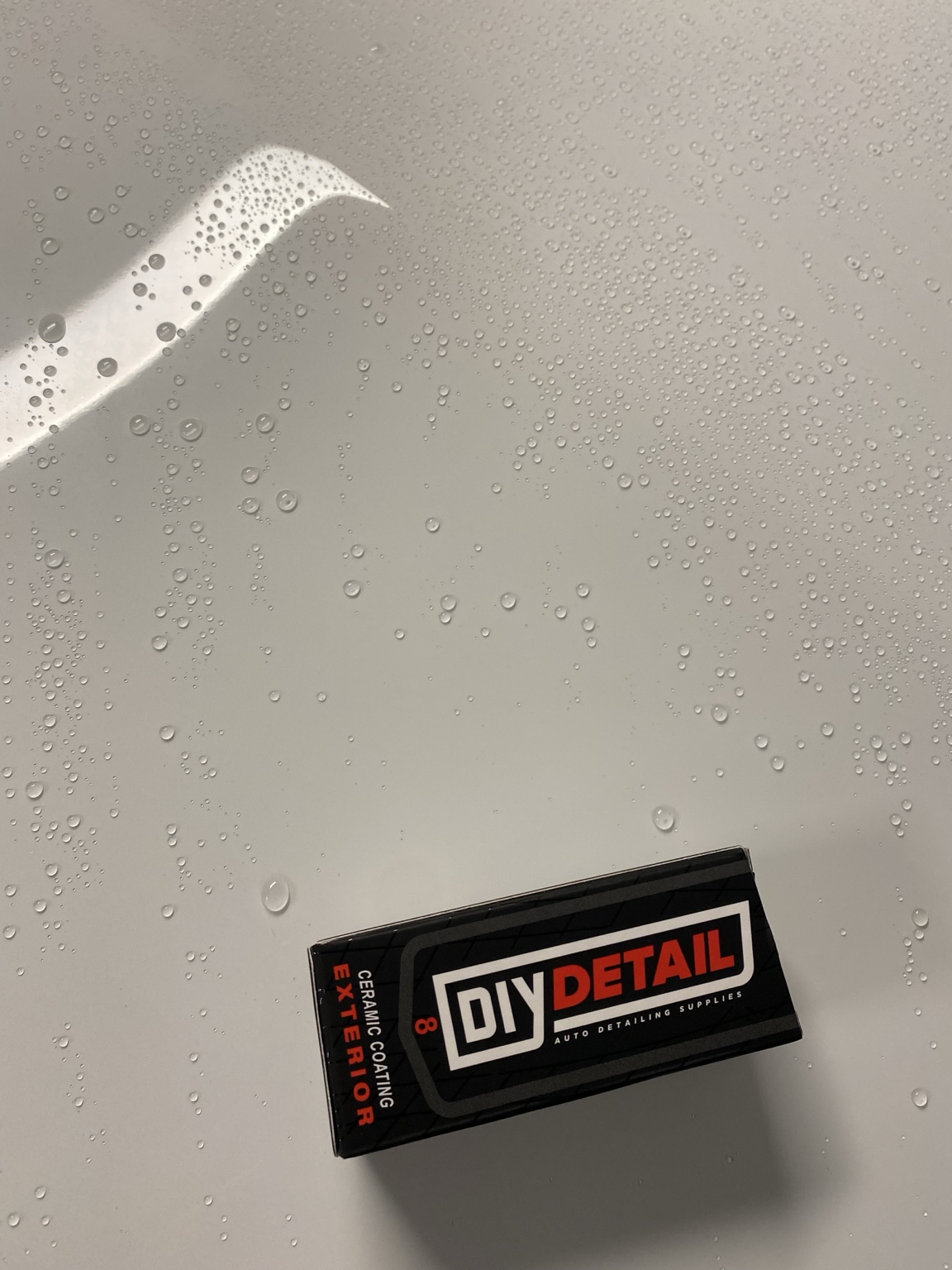 Water beading on white painted surface beside ceramic coating product box.